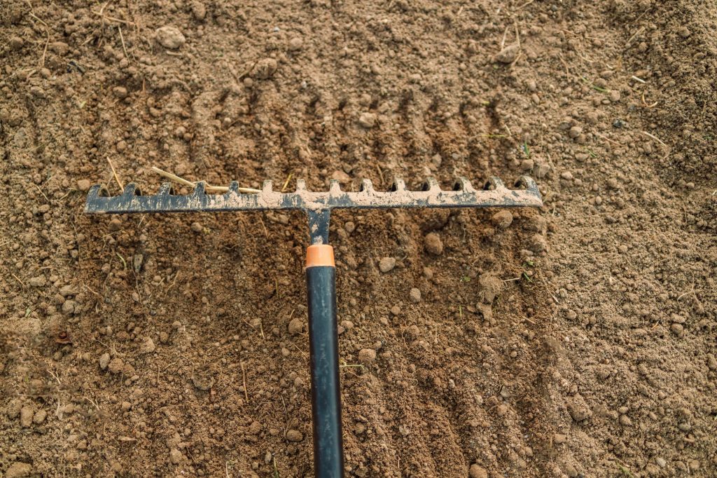 Close up of an new metal garden rake cleaning earth at spring time. Seasonal work